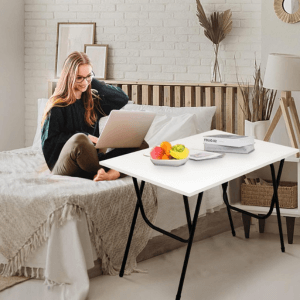 Woman using white folding laptop desk table while sitting on bed in modern bedroom